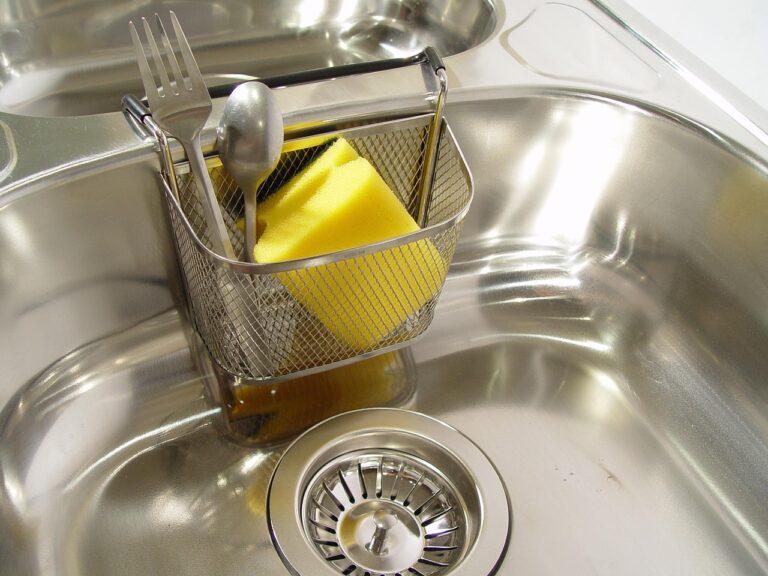 Clogged stainless steel kitchen sink filled with standing water and drain cleaning tools nearby